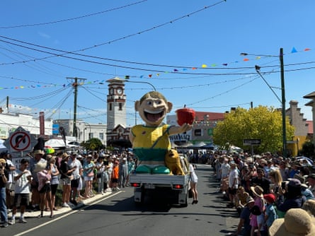A giant model of a smiling man holding a red apple on the back of a ute