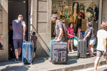 People, including young children, wheel their suitcases to the door of an apartment building in Barcelona next to a clothes shop
