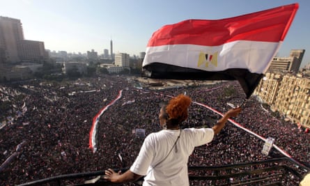 A woman waves the Egyptian flag from a balcony as tens of thousands gather in Tahrir Square in Cairo a week after Hosni Mubarak resigned.