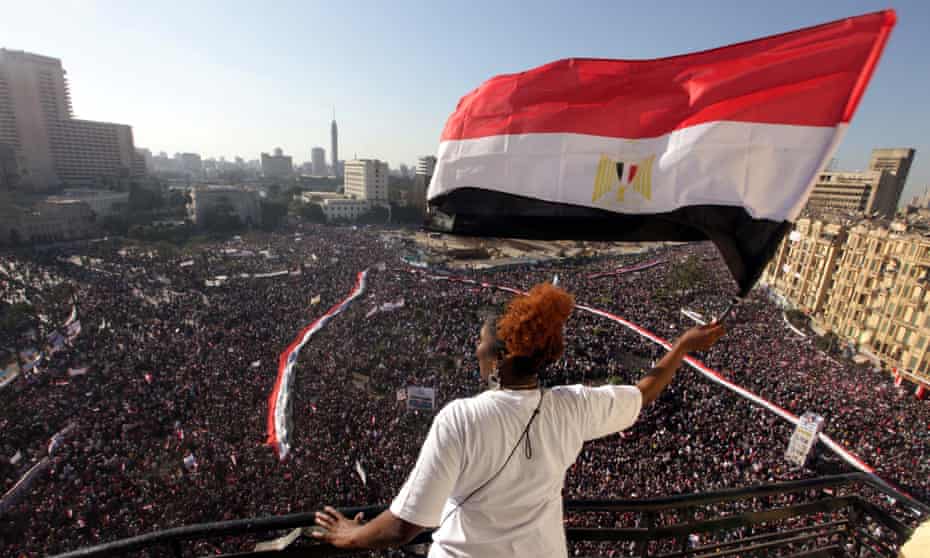 Una mujer ondea la bandera egipcia desde un balcón mientras decenas de miles se reúnen en la plaza Tahrir en El Cairo una semana después de que Hosni Mubarak renunciara.