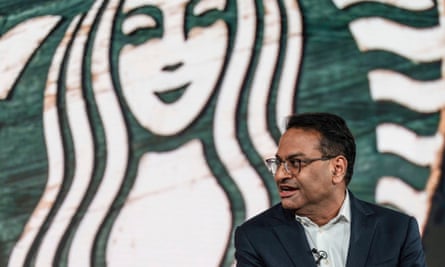 Laxman Narasimhan sitting in smiling at. a meeting or conference in front of a very large Starbucks logo