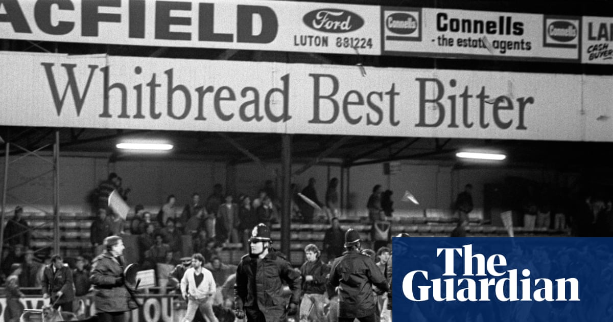 Aficionados de fútbol en una grada inglesa en los años ochenta, con un cartel que prohíbe la venta de alcohol en el estadio.