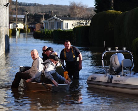 Four men in a dinghy helped by a man standing up to his ankles in a flooded road beside a small motor boat