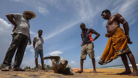 Four south Asian men stand on a beach looking at a dead turtle on its back