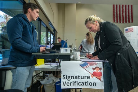 Man stands on one side of table outdoors and woman across from him signs a piece of paper.