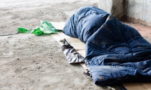 Homeless man sleeping in sleeping bag on cardboard