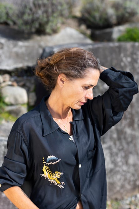 Portrait of Sarah Green, outdoors in front of rocks earing a dark shirt with a tiger embroidered on it and running her hand through her hair