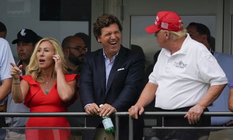 Marjorie Taylor Greene stands at a railing next to Tucker Carlson and Donald Trump during a golf tournament.