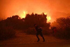 Bright flames emanating from a bush turn the air orange as firefighters try to extinguish the fire