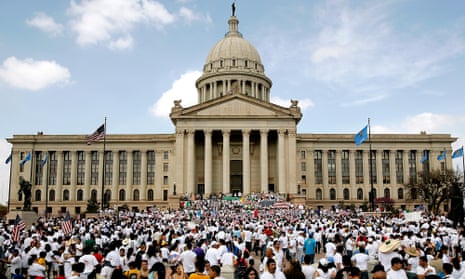 Long, white-stone building with taller columns in front and cupola beyond, with hundreds of people in white T-shirts gathered in front.