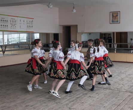 Children in traditional costumes dance in a circle holding hands in a large room