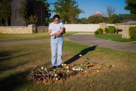 Woman stands in a cemetery holding a baby