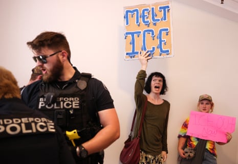 Two people hold anti-ICE signs as police stand nearby
