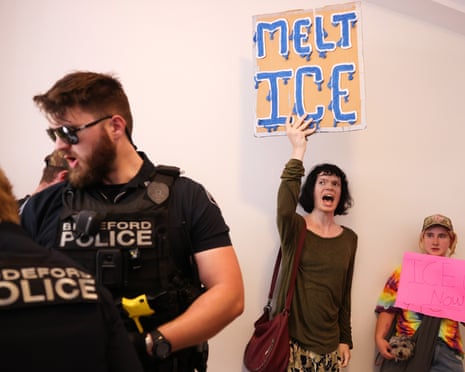 Two people hold anti-ICE signs as police stand nearby