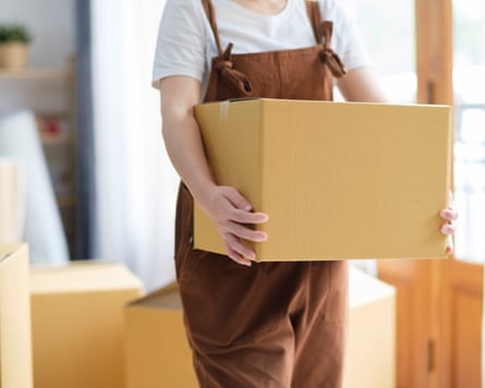 A person wearing brown dungarees carries a cardboard box while moving home