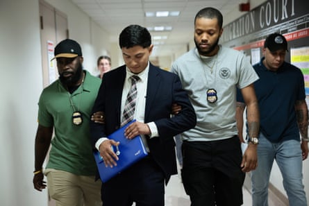 Two men escort another a man through a hallway