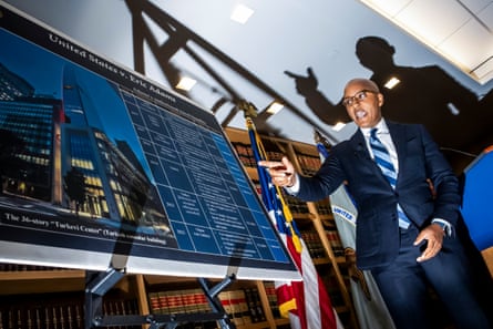 a man in a blue suit and tie speaks while pointing to a chart