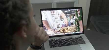 A woman seen from behind watches a laptop with an image of a shopkeeper selling pangolin scales.