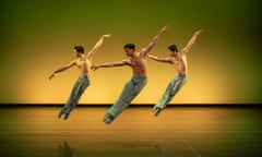 three young male dancers midair, arms raised in unison, legs pointed sharply to the left, against a bright yellow background