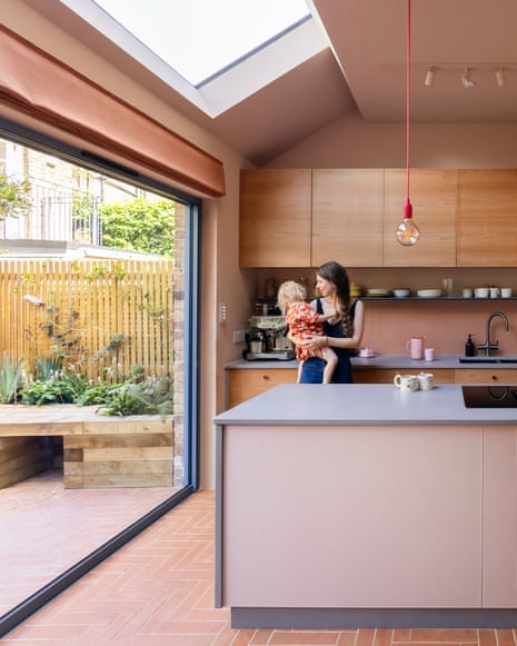 A kitchen with clean lines and muted pink decor, open on to a paved garden.