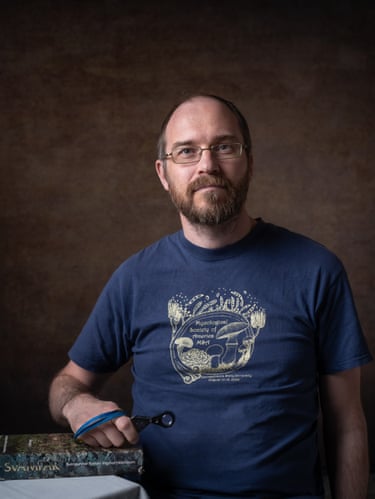 A man holds a magnifying lens and rests his arm on a book