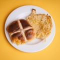 An M&S extremely cheesy cheddar and red leicester hot cross bun, sliced, toasted and buttered, on a white plate