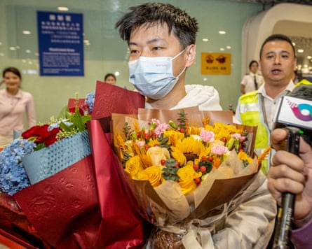Zhao Xintong holding bunches of flowers walks past a person holding a microphone