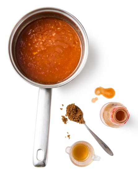 Coating sauce in a pan with a spoon full of spice, a bottle of hot sauce and a measuring jug of vinegar, to taste