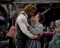 A woman in a grey dress looking lovingly at a man in a white shirt, surrounded by other people