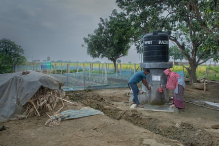 A man and a woman collect water from a tube well next to a crop field.