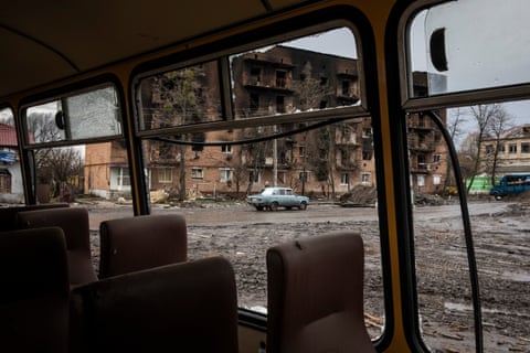 The charred exterior of a residential building viewed from inside the remains of a bus
