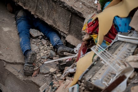 A man’s legs and boots can be seen poking out from under a crevice in a collapsed wall
