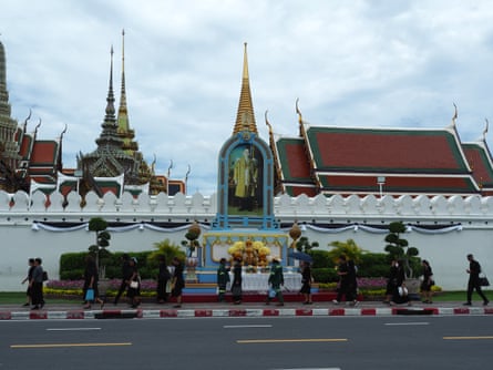 People walk along a pavement outside the Grand Palace