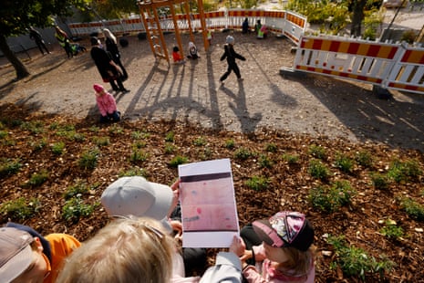 A piece of paper with a design on it is held by someone who is mostly out of shot, surrounded by children. Other children can be seen playing beyond