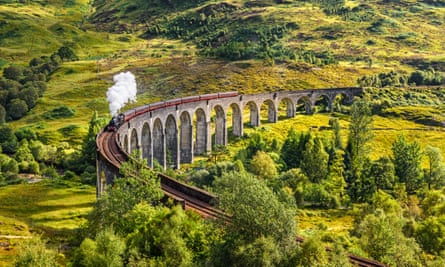 A train crosses the viaduct, surrounded by green hills