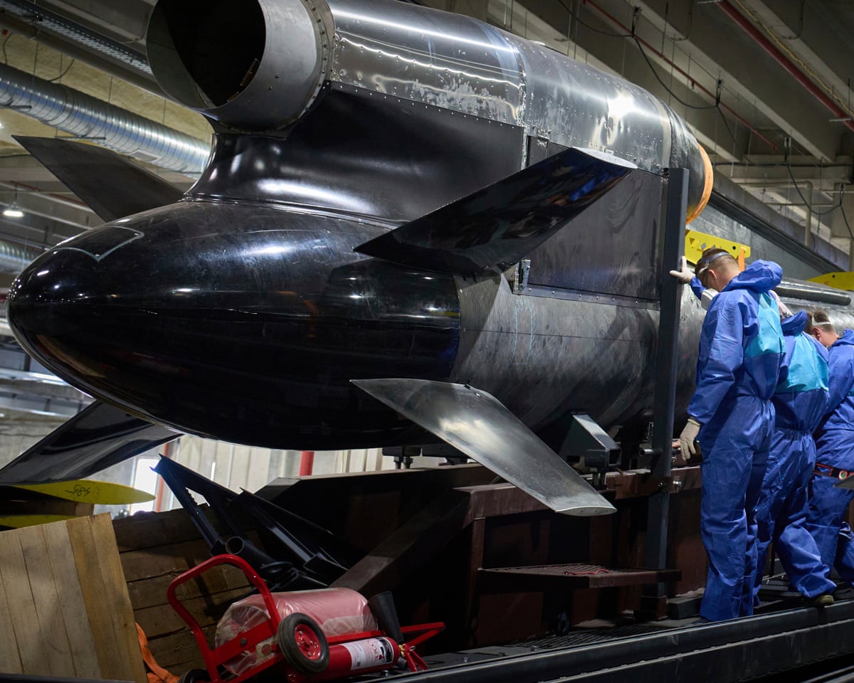 People in blue Hazmat suits next to a very large steel missile