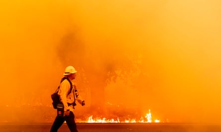 A Pacific Gas and Electric firefighter walks down a road as flames approach in Fairfield, California.
