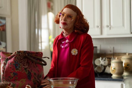 A red-haired woman wearing pink glasses stands in a kitchen