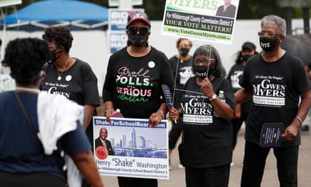 A line our four Black older women wearing black facemasks and black T-shirts holding political signs outdoors.