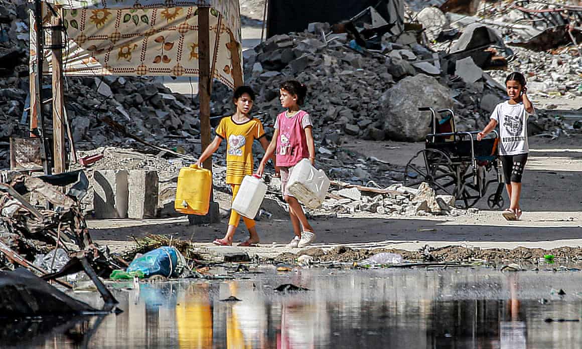 Girls walking past a puddle of sewage carrying plastic jerry cans