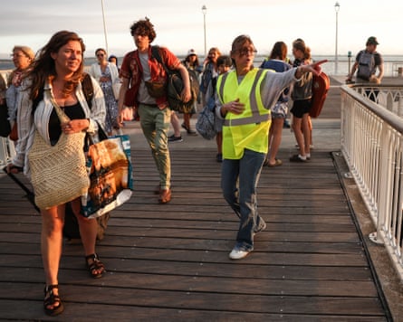 A volunteer in hi-vis directs holidaymakers fleeing Cap Ferret as they arrive in Arcachon by boat.