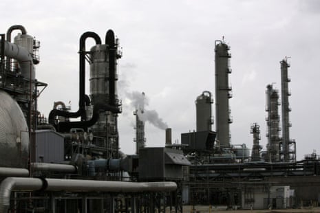 Multiple industrial towers and pipes at a chemical refinery emit steam against an overcast sky