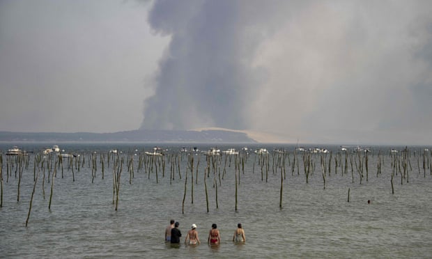 Tourists in south-western France on Monday look at the plume of dark smoke over the Dune of Pilat due to a wildfire.