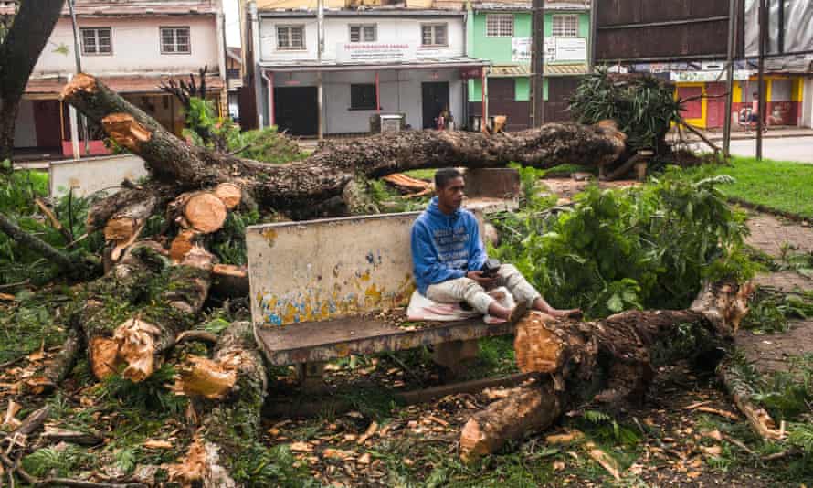 A man sits on a bench amid trees that were uprooted and that fell on a public garden following the passage of cyclone Batsirai.