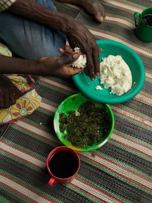 hands shape a ball of ugali porridge from a bowl with a plate of a green leaf vegetable beside it