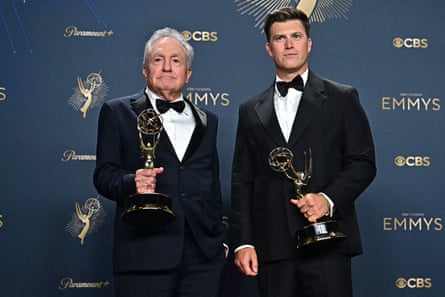 Two men in tuxes hold Emmy statues.