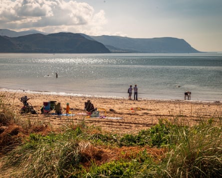 People on a beach with grasses behind and headlands in the distance