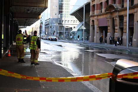Two workers in yellow vests stand on a street flooded by water