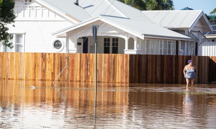 A woman stands on a street corner in Ballina with flood waters around her ankles and a white house behind her