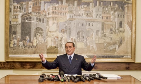 Silvio Berlusconi gesturing with his hands, in front of a large artwork.